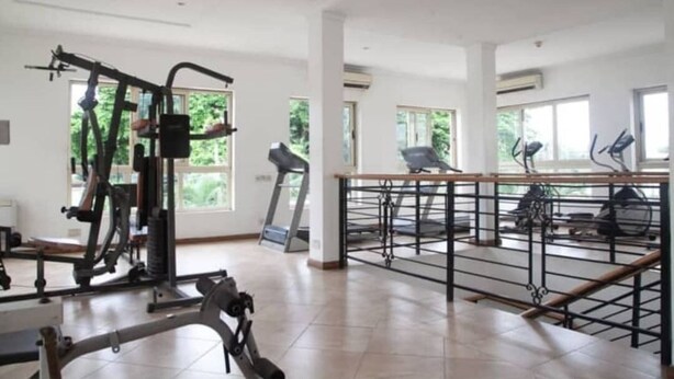 A spacious gym with various exercise equipment, large windows, and a wooden railing. - Mulliner Towers (Lagos)