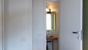 Ein Badezimmer mit weißer Tür, einem Spiegel und einem Waschbecken.