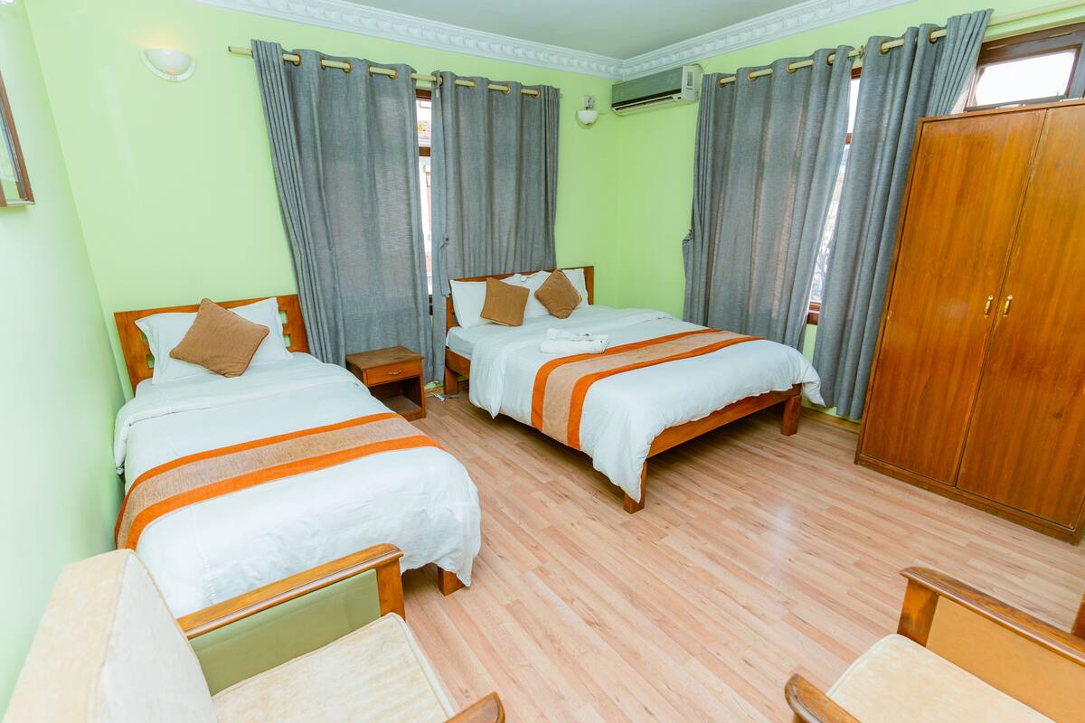 A hotel room with two beds, wooden headboards, a wardrobe, and a small bedside table.