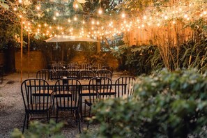 An outdoor seating area with tables and chairs, string lights overhead, and a bamboo backdrop. - Cloud 9 Garden (Gokarneshwar)