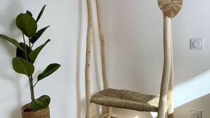 A wooden chair with a woven seat and backrest, a small wooden stool, and a potted plant with broad leaves.