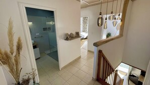 A modern interior with a staircase, a glass door leading to a bathroom, and pendant lights.