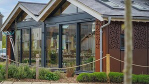 A modern building with large glass windows and a sloped roof. - Eider Cottage: Lakeside Escape with Spa Access (Cirencester)
