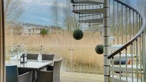 A spiral staircase leading to a deck with outdoor furniture and a view of residential buildings. - Eider Cottage: Lakeside Escape with Spa Access (Cirencester)