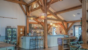 A rustic interior with exposed wooden beams, a bar area with stools, and a seating area with tables. - Eider Cottage: Lakeside Escape with Spa Access (Cirencester)