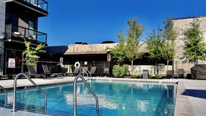 A swimming pool with a metal ladder, lounge chairs, and a fenced area with trees and a building in the background. - Midtown Pool Condo · 2BR Sleeps 6 · Honky Tonk (Nashville)