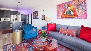 A modern living room with a grey sofa, red cushions, a blue armchair, and a glass coffee table with a vase of flowers. - Midtown Pool Condo · 2BR Sleeps 6 · Honky Tonk (Nashville)