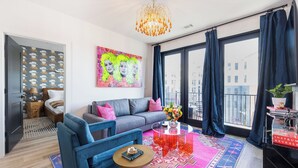 A modern living room with a sofa, armchair, and coffee table, a colorful rug, and a large window with curtains.