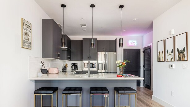 A modern kitchen with dark cabinets, stainless steel appliances, and a central island with bar stools.