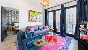 Ein modernes Wohnzimmer mit einer Couch, Sesseln, einem Couchtisch und einem großen Fenster mit Vorhängen.