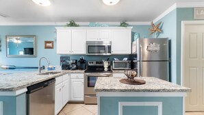 A kitchen with white cabinets, a microwave, a stove, and a refrigerator. - 🌴🌞Walk to Beach | Prime Location | 2BR Grand Caribbean 115🌞🌴 (Orange Beach)