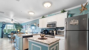 A modern kitchen with a central island, white cabinets, stainless steel appliances, and a 'Welcome' sign on the refrigerator. - 🌴🌞Walk to Beach | Prime Location | 2BR Grand Caribbean 115🌞🌴 (Orange Beach)