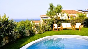 Une piscine avec vue sur la mer, entourée d’une pelouse bien entretenue et d’un bâtiment doté d’un toit en tuiles.