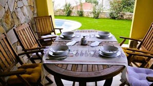 Une table à manger pour six personnes, avec des chaises, un mur en pierre et une vue sur une piscine et un jardin.