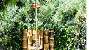 Un espace extérieur entouré de murs en pierre, agrémenté d’une mangeoire à oiseaux suspendue et de jardinières en bambou.
