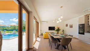 A modern kitchen with a dining area, large windows, and a view of a swimming pool.