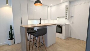 A modern kitchen with white cabinets, a wooden island with bar stools, a built-in oven, and a pendant light.