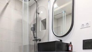A modern bathroom with a glass shower enclosure, a wooden vanity with a black countertop, and a round mirror.