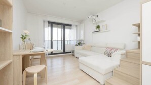 Una sala de estar moderna con un sofá blanco, una mesa de comedor con sillas y una escalera.