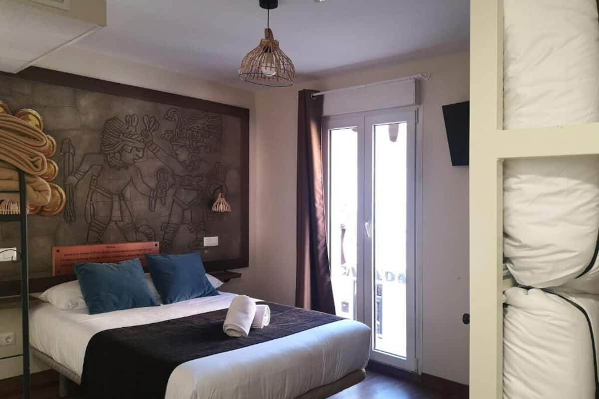 Quarto com cama grande, um mural na parede, luminária pendente e vista por uma porta deslizante.
