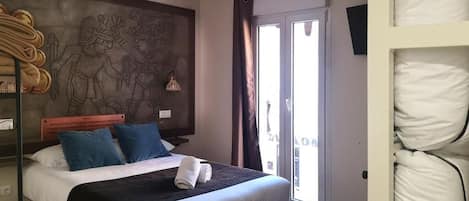 Un dormitorio con una cama grande, un mural en la pared, una lámpara colgante y vistas a través de un ventanal corredero.