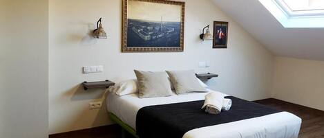 Un dormitorio con una cama, un tragaluz, un cuadro enmarcado y una lámpara de pared.