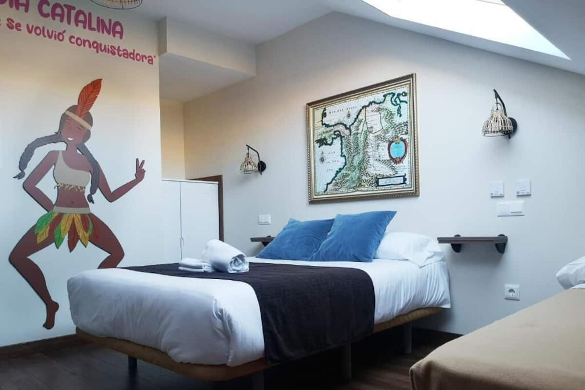 Quarto de hotel com uma cama, um mapa de parede e um mural de uma figura histórica.