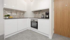 Cocina compacta con armarios blancos, salpicadero estampado y horno empotrado.