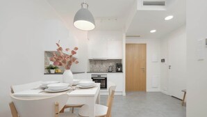 Una cocina moderna con armarios blancos, una cafetera y un comedor con mesa y sillas blancas.