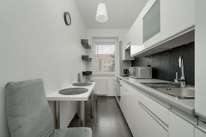 A compact kitchen with white cabinets, a microwave, a kettle, and a sink.