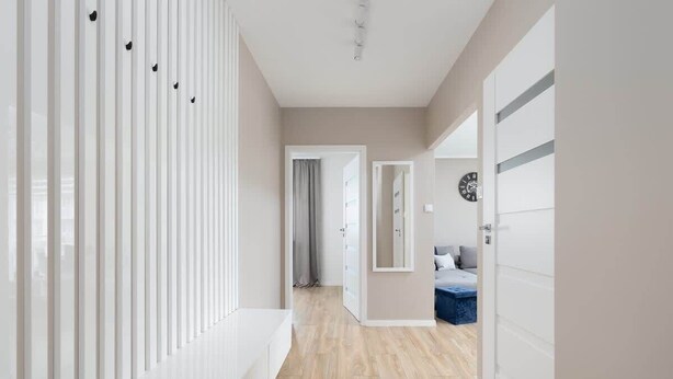 A hallway with a wooden floor, white walls, and a door leading to a bedroom with a bed and a dresser.