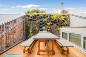 A rooftop terrace with a long table and benches, surrounded by a variety of plants and a brick wall. - Victorian City-Fringe 3lvl Home @Carlton Lifestyle (Carlton)