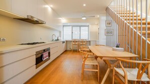 Una cucina moderna con mobili bianchi, un tavolo da pranzo in legno e una scala con ringhiere in metallo.