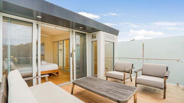Un balcone moderno all'aperto con un tavolo di legno, due divani e una poltrona.