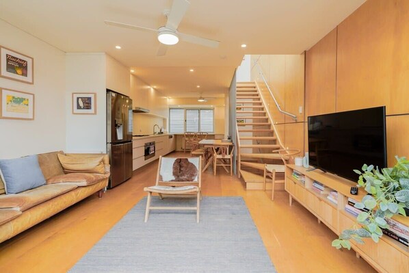 A modern living room with a sofa, a coffee table, a TV, and a staircase leading to an upper level. - Victorian City-Fringe 3lvl Home @Carlton Lifestyle (Carlton)