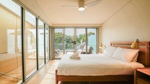 Una camera da letto moderna con un letto grande, una ventola a soffitto e vista all'esterno tramite ampie porte scorrevoli in vetro.