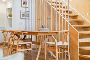 Eine Holztreppe mit minimalistischem Design, ein Essbereich mit einem Holztisch und Stühlen sowie ein kleiner Topfpflanze auf dem Tisch.