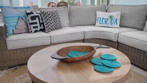 Un sofá modular con cojines estampados, una bandeja de madera con posavasos y una mesa de centro de mimbre.
