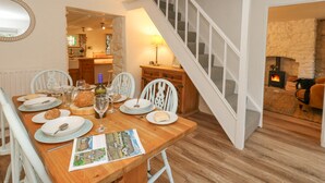 Un comedor con una mesa de madera preparada para cuatro personas, una chimenea y una escalera que lleva a otra habitación.