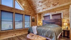 Ein Schlafzimmer einer Holzhütte mit Bett, Bank und großen Fenstern.