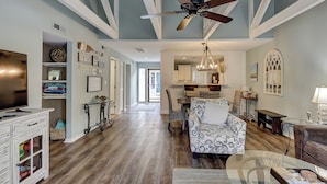 A spacious living room with hardwood floors, a ceiling fan, and a dining area with a chandelier.