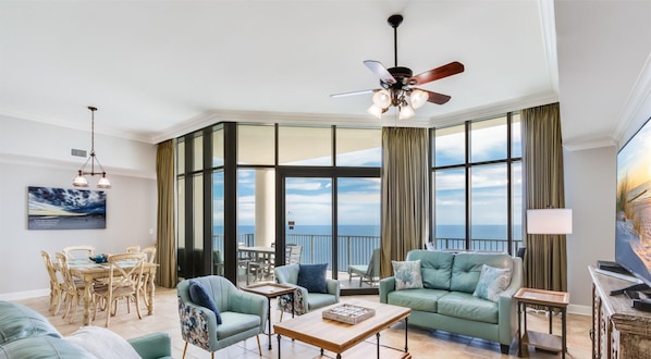 Ein geräumiges Wohnzimmer mit großem Fenster und Meerblick, Deckenventilator sowie Essbereich mit Stühlen und Tisch.