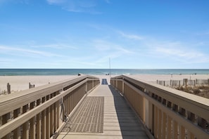 Une promenade en bois qui mène à une plage, avec un ciel dégagé.