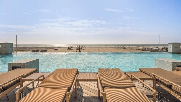 Une piscine avec des chaises longues, une vue sur la plage et un ciel dégagé.