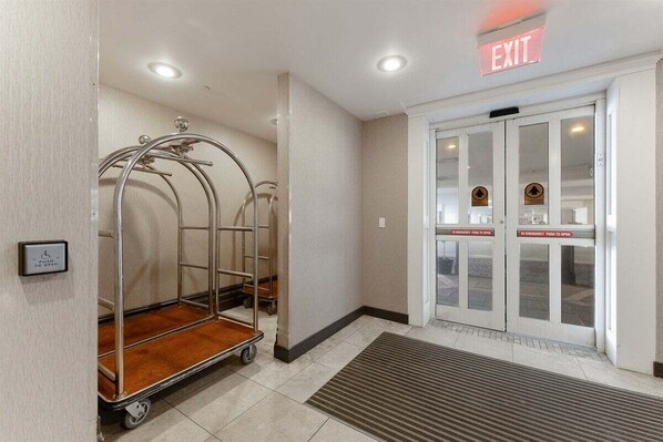A hotel entrance with an exit sign, a push-to-open emergency door, and a luggage cart.