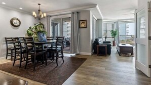 Un vaste espace de vie comprenant une table à manger, des chaises, un lustre et une vue sur un balcon extérieur, accessible par une porte vitrée.