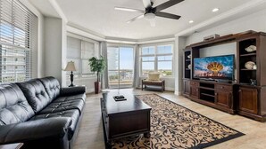 Un salon avec un canapé en cuir, une table basse, un téléviseur posé sur un meuble en bois et un tapis à motifs.