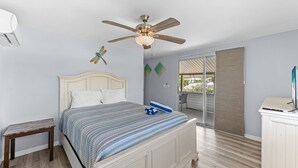 Une chambre Ă coucher avec un lit, un ventilateur de plafond, une petite table et une vue sur lâextĂ©rieur.