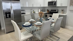 A modern kitchen with white cabinets, stainless steel appliances, and a glass dining table set for four.