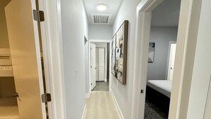 A narrow hallway with light-colored wooden flooring, white walls, and a ceiling with recessed lighting.